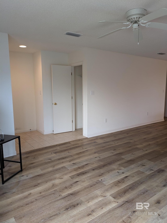 unfurnished room featuring light wood-type flooring, a ceiling fan, visible vents, and a textured ceiling