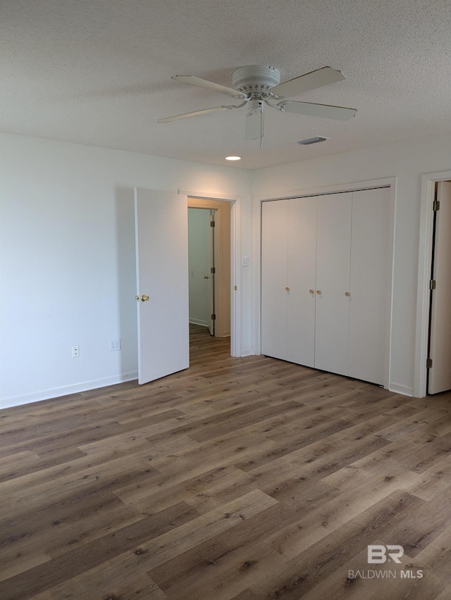 unfurnished bedroom featuring a closet, baseboards, ceiling fan, a textured ceiling, and wood finished floors