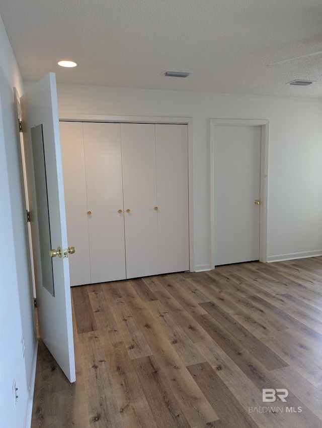 unfurnished bedroom featuring a textured ceiling, wood finished floors, a closet, and visible vents