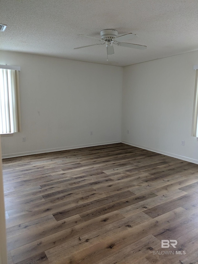 empty room with dark wood-style floors, a textured ceiling, visible vents, and ceiling fan