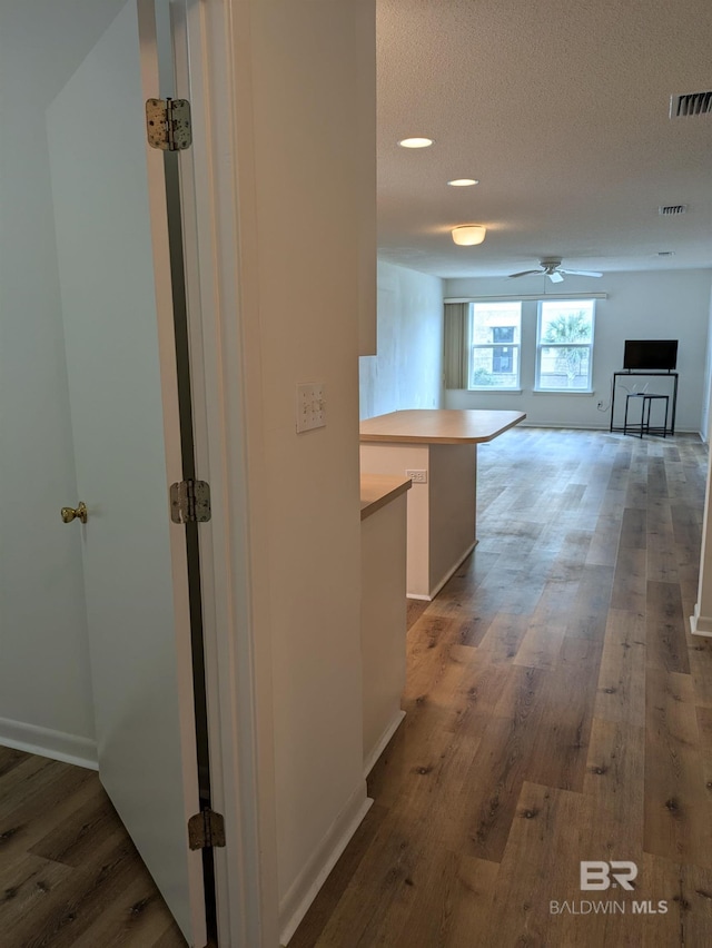 corridor featuring visible vents, baseboards, a textured ceiling, and wood finished floors