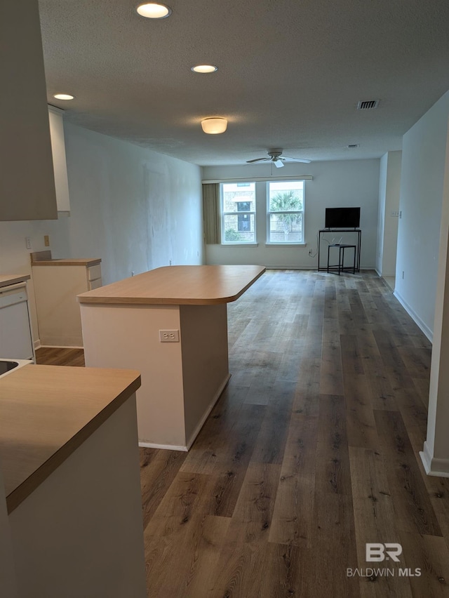 kitchen featuring visible vents, a center island, white cabinets, dark wood-style flooring, and a ceiling fan