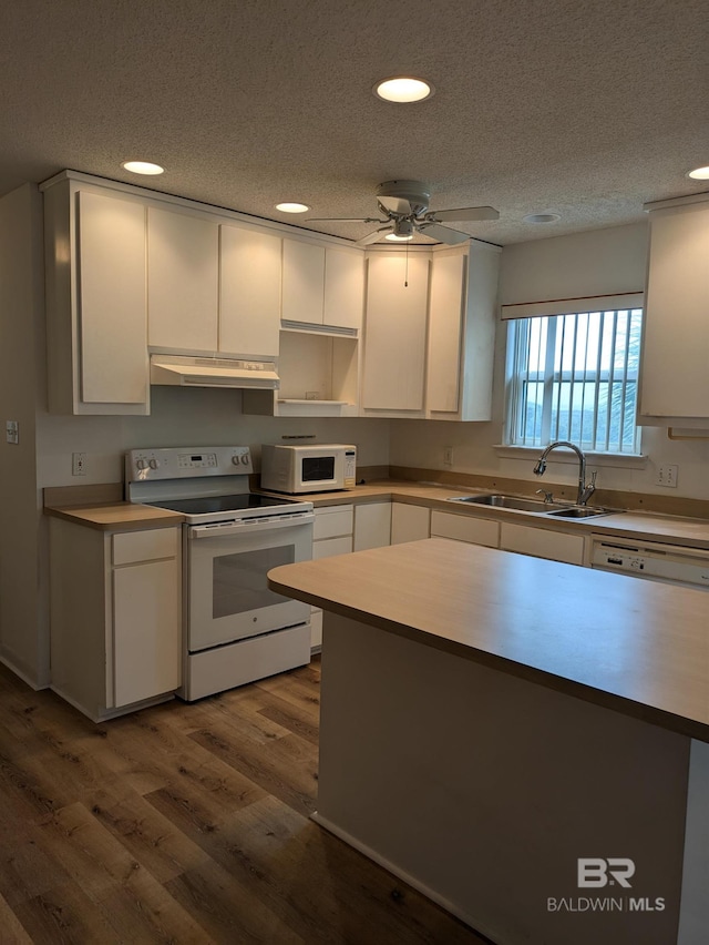 kitchen with under cabinet range hood, a sink, white appliances, a textured ceiling, and white cabinetry
