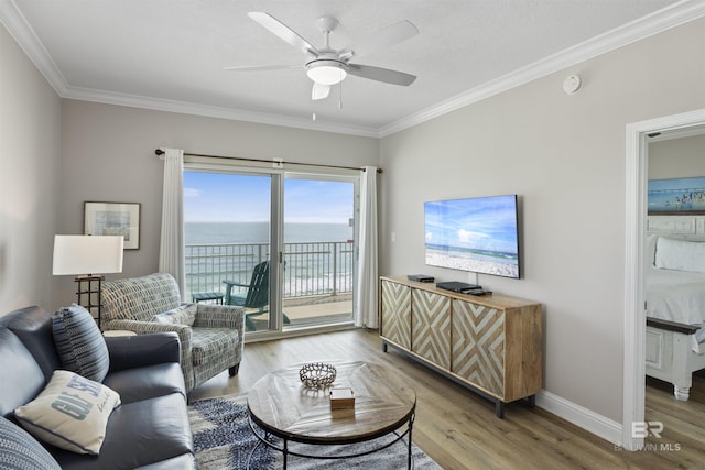 living room featuring a ceiling fan, crown molding, baseboards, and light wood-type flooring