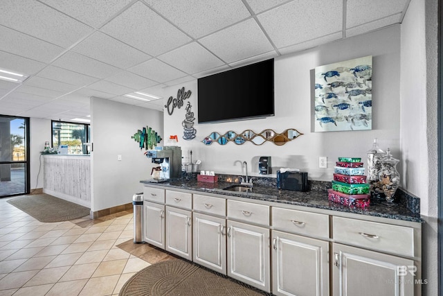 bar with a drop ceiling, light tile patterned flooring, sink, and dark stone counters