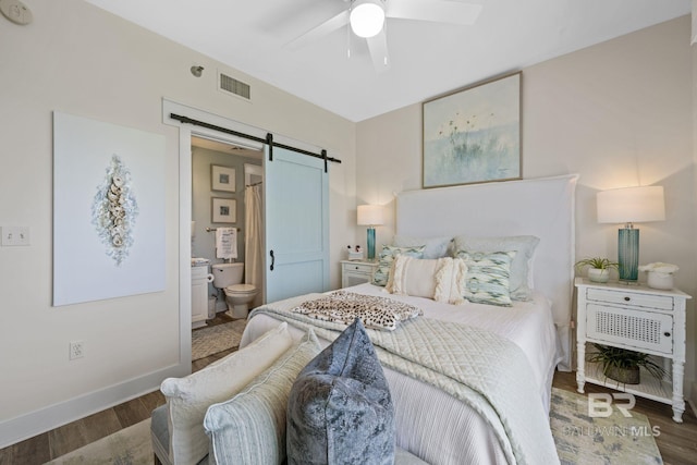 bedroom with a barn door, ceiling fan, connected bathroom, and dark hardwood / wood-style floors