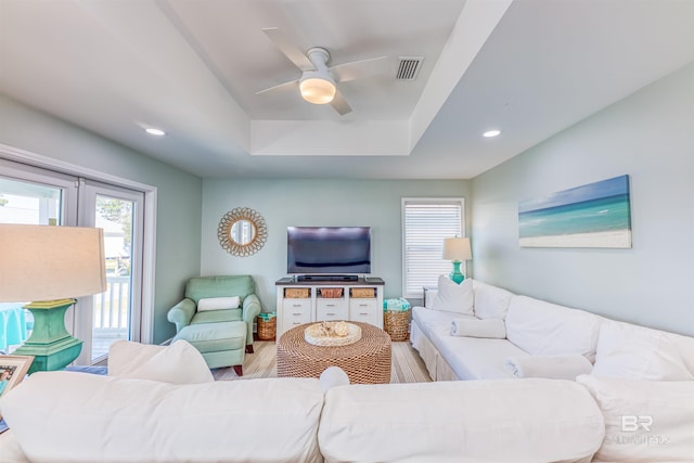 living area with a tray ceiling, plenty of natural light, wood finished floors, and visible vents