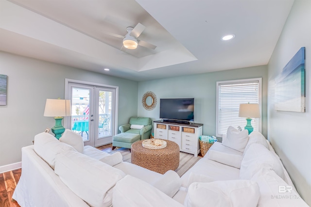 living room with ceiling fan, a tray ceiling, french doors, light wood-style floors, and recessed lighting