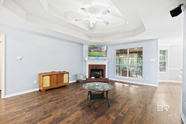 living room with a raised ceiling, ceiling fan, dark hardwood / wood-style flooring, and a fireplace