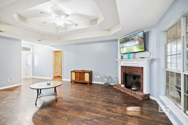 living room featuring a raised ceiling, ceiling fan, dark hardwood / wood-style flooring, and a brick fireplace