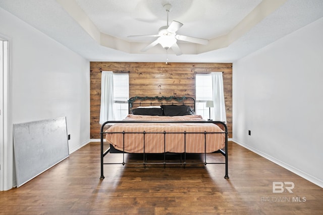 bedroom with a tray ceiling, ceiling fan, multiple windows, and dark hardwood / wood-style floors