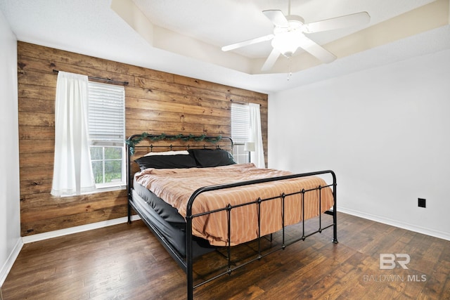 bedroom featuring ceiling fan, dark wood-type flooring, a raised ceiling, and wooden walls