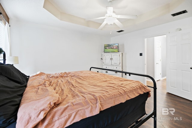 bedroom with dark hardwood / wood-style floors, ceiling fan, and a raised ceiling