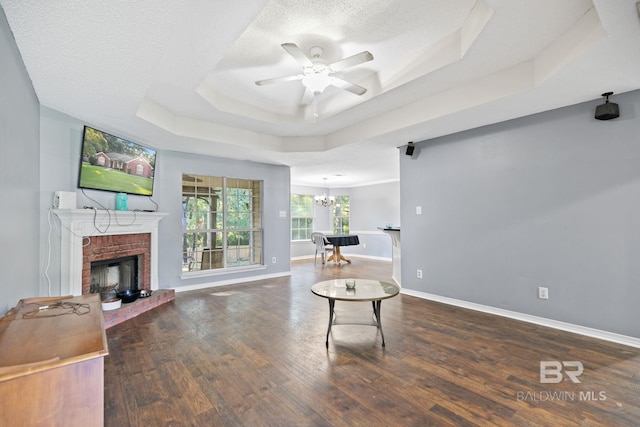 living area featuring ceiling fan with notable chandelier, a textured ceiling, a raised ceiling, a fireplace, and dark hardwood / wood-style floors