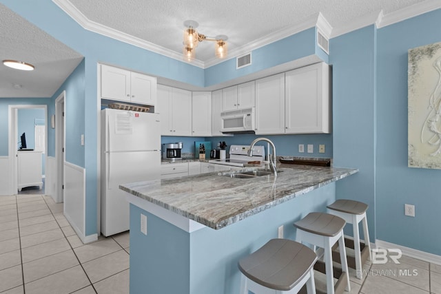 kitchen featuring white appliances, a kitchen breakfast bar, a peninsula, crown molding, and a sink