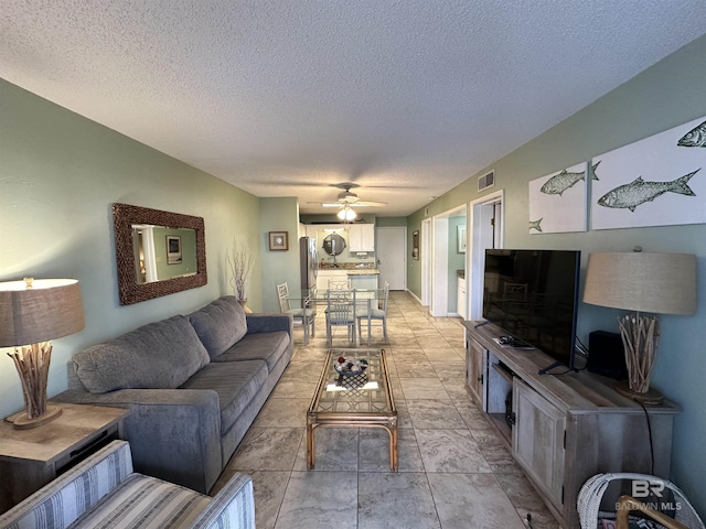 living room featuring visible vents, ceiling fan, and a textured ceiling