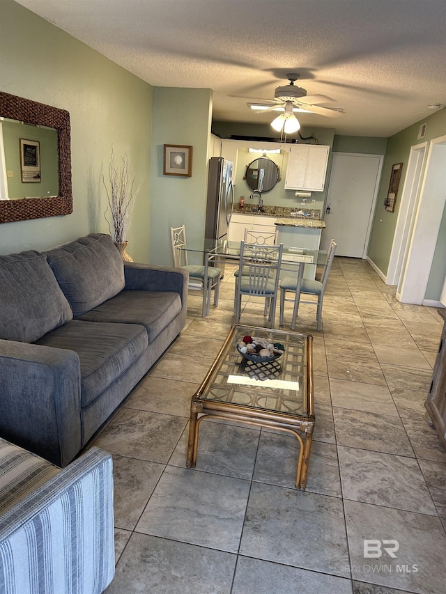 living area featuring ceiling fan, baseboards, and a textured ceiling