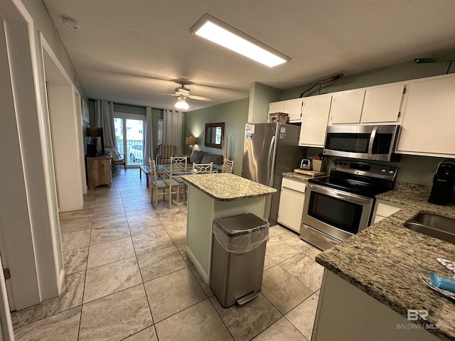 kitchen with ceiling fan, a kitchen island, light stone counters, stainless steel appliances, and white cabinetry