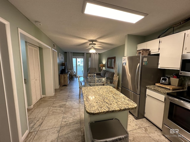 kitchen with a textured ceiling, stainless steel appliances, a ceiling fan, white cabinets, and a center island