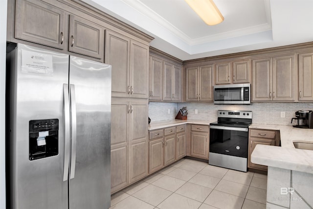 kitchen with stainless steel appliances, tasteful backsplash, light tile patterned floors, a tray ceiling, and ornamental molding
