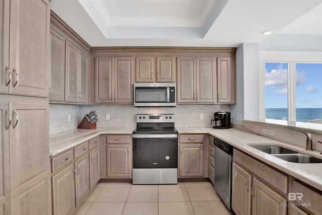 kitchen featuring appliances with stainless steel finishes, a sink, a tray ceiling, decorative backsplash, and light stone counters