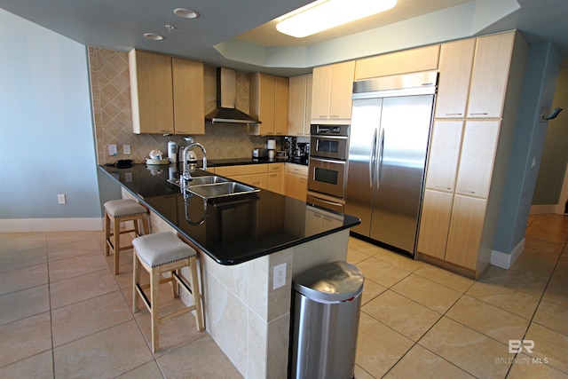 kitchen featuring kitchen peninsula, appliances with stainless steel finishes, a breakfast bar area, tasteful backsplash, and wall chimney exhaust hood