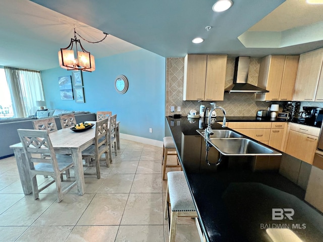 kitchen featuring hanging light fixtures, light brown cabinets, backsplash, wall chimney range hood, and a notable chandelier