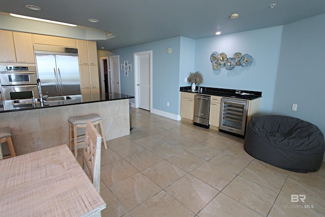 kitchen featuring beverage cooler, light brown cabinets, light tile floors, a breakfast bar area, and stainless steel appliances