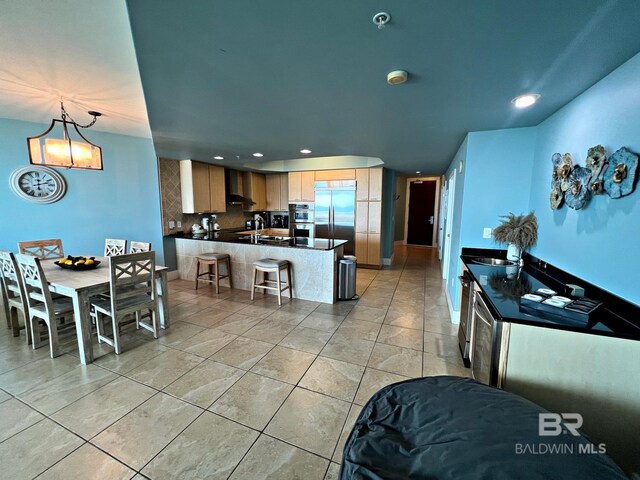 kitchen with appliances with stainless steel finishes, light tile flooring, wall chimney range hood, kitchen peninsula, and pendant lighting