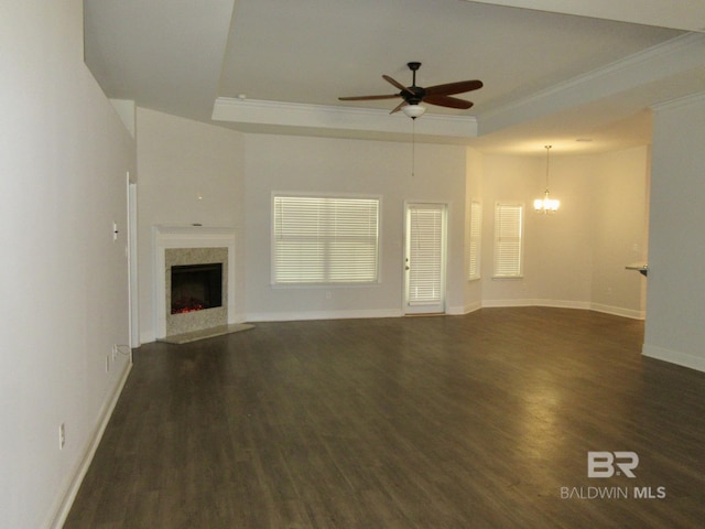 unfurnished living room featuring dark wood-type flooring, ceiling fan with notable chandelier, a fireplace, and a tray ceiling