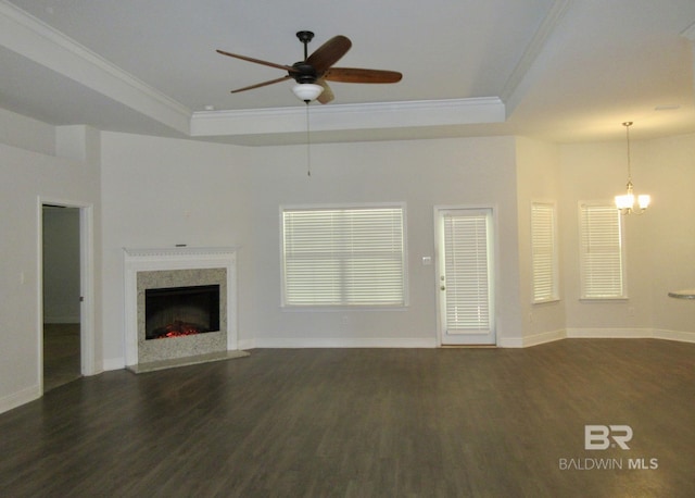 unfurnished living room featuring dark wood-type flooring, ornamental molding, ceiling fan with notable chandelier, and a tray ceiling