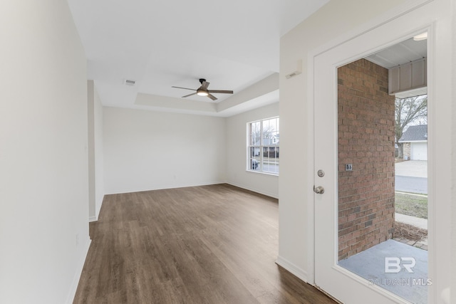 unfurnished room with a tray ceiling, dark wood-type flooring, and ceiling fan