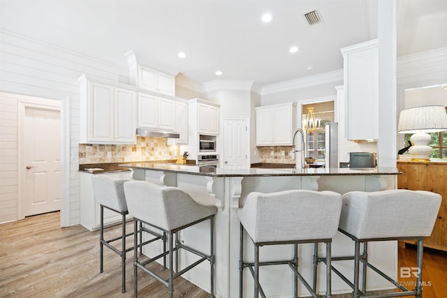 kitchen with a breakfast bar, crown molding, light hardwood / wood-style flooring, appliances with stainless steel finishes, and white cabinetry