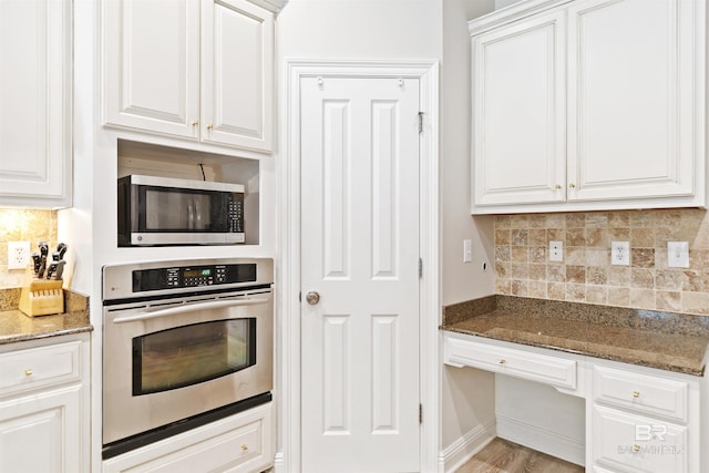 kitchen with dark stone countertops, white cabinetry, stainless steel appliances, and light wood-type flooring