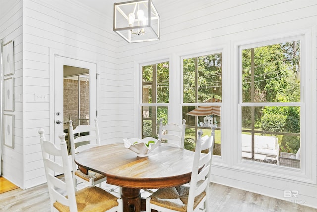 dining space with an inviting chandelier, wood walls, plenty of natural light, and light wood-type flooring