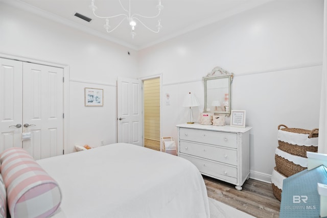 bedroom featuring dark wood-type flooring, ornamental molding, a closet, and a notable chandelier