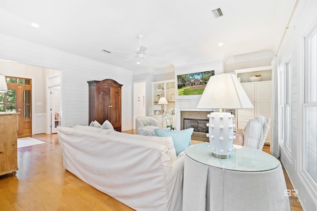 living room featuring crown molding, a fireplace, light hardwood / wood-style floors, and ceiling fan