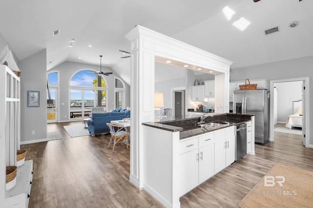 kitchen featuring stainless steel appliances, vaulted ceiling, white cabinets, light wood-type flooring, and dark stone countertops