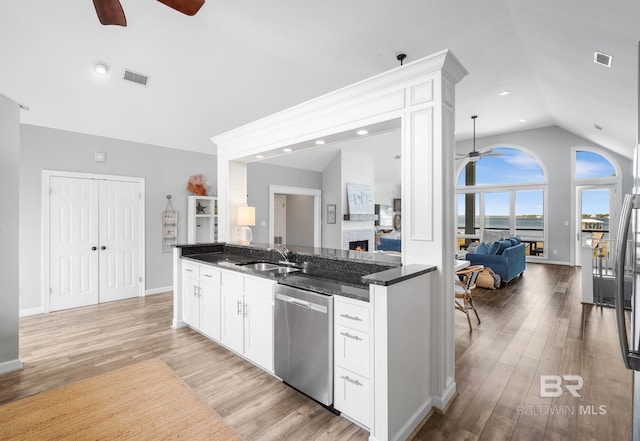 kitchen with white cabinetry, dark stone counters, stainless steel dishwasher, light wood-type flooring, and vaulted ceiling