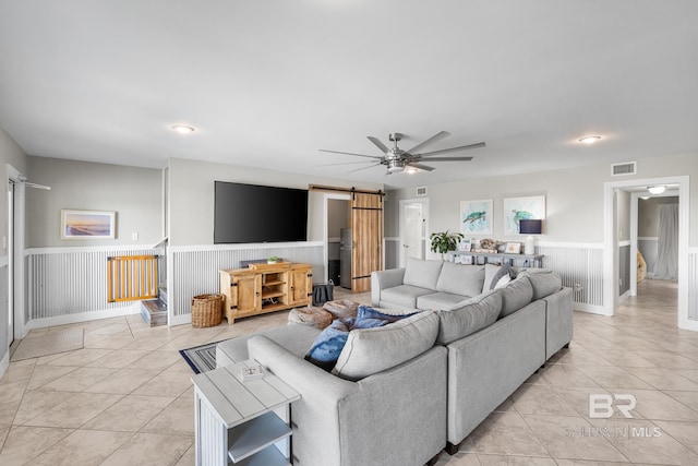 living room with a barn door, ceiling fan, and light tile patterned floors