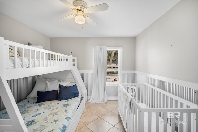 tiled bedroom featuring a nursery area and ceiling fan