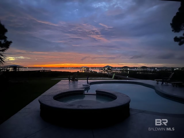 pool at dusk with an in ground hot tub and a water view