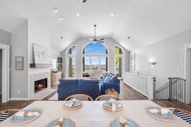 dining space featuring dark wood-type flooring, high vaulted ceiling, ceiling fan, and a fireplace