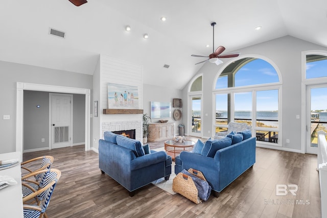 living room featuring a water view, ceiling fan, dark hardwood / wood-style floors, high vaulted ceiling, and a brick fireplace