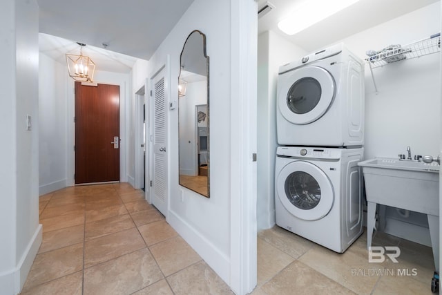 washroom featuring baseboards, laundry area, stacked washer and clothes dryer, light tile patterned flooring, and a notable chandelier