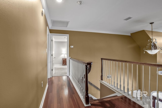 corridor with dark hardwood / wood-style flooring, ornamental molding, and a chandelier