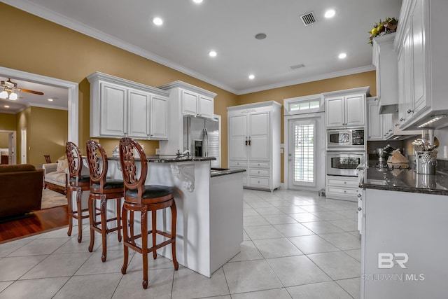 kitchen with ceiling fan, a breakfast bar area, stainless steel appliances, light tile flooring, and white cabinetry