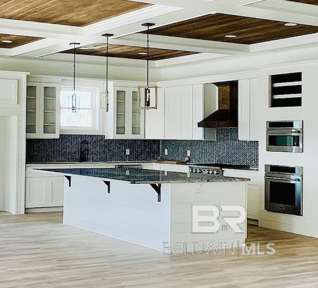 kitchen with wall chimney exhaust hood, white cabinets, tasteful backsplash, and a kitchen bar