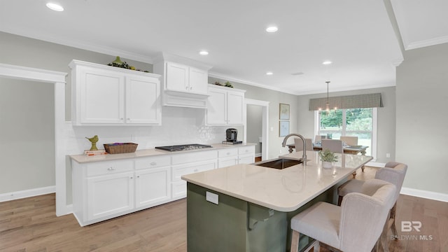 kitchen featuring light wood-type flooring, crown molding, white cabinets, decorative backsplash, and a sink