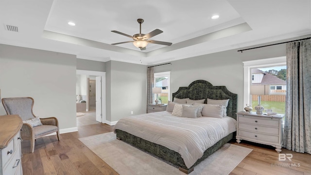 bedroom with a raised ceiling, light wood-style floors, visible vents, and recessed lighting